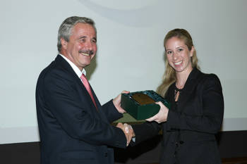 A woman and a man shake hands and smile for a commemorative photo as the woman receives an honorary award
